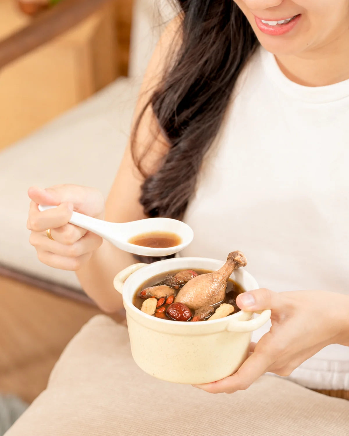 女生窝在沙发上，捧着一碗热汤慢慢喝